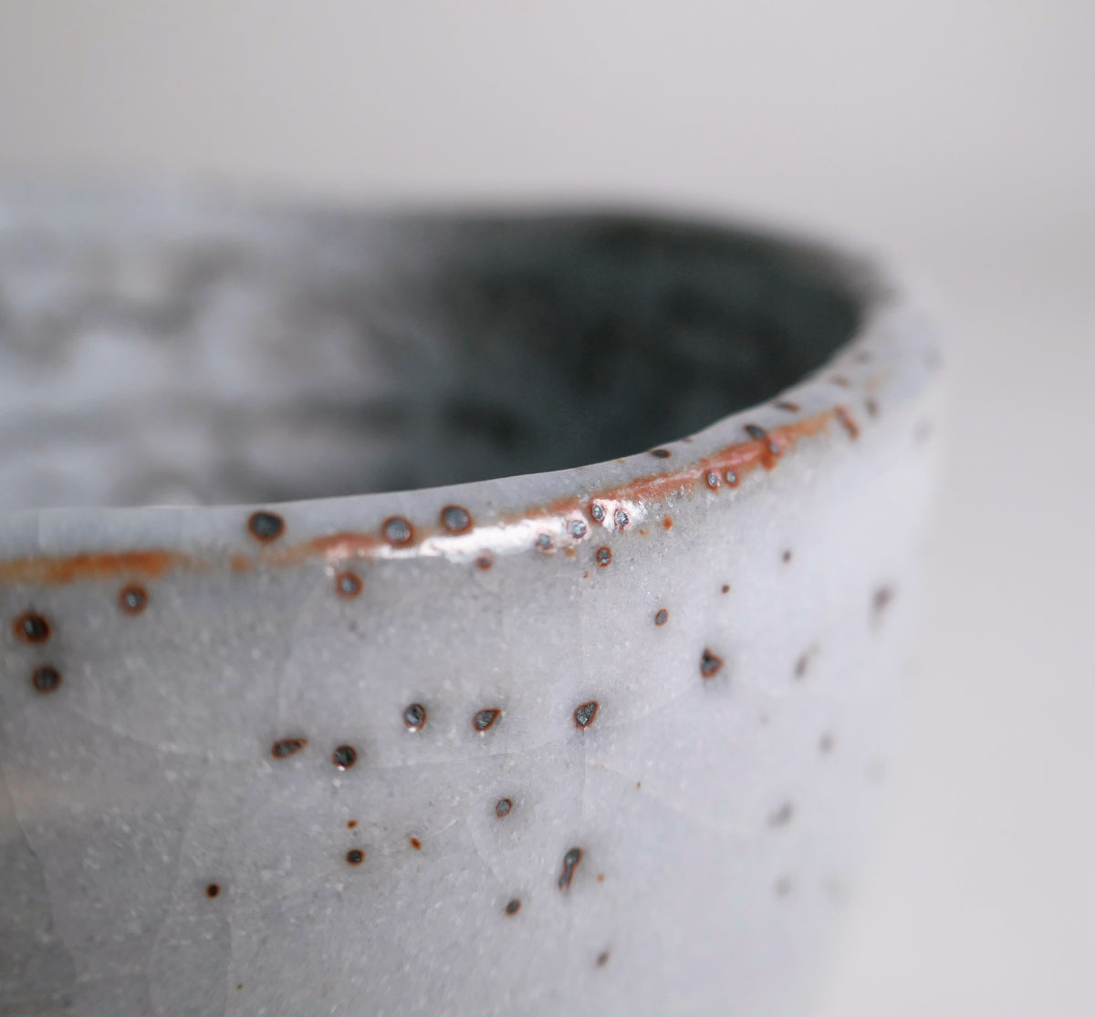 Détail du bord du chawan Shino avec yuzuhada et nuances ferrugineuses hi-iro rouge-orangé produites à la cuisson.