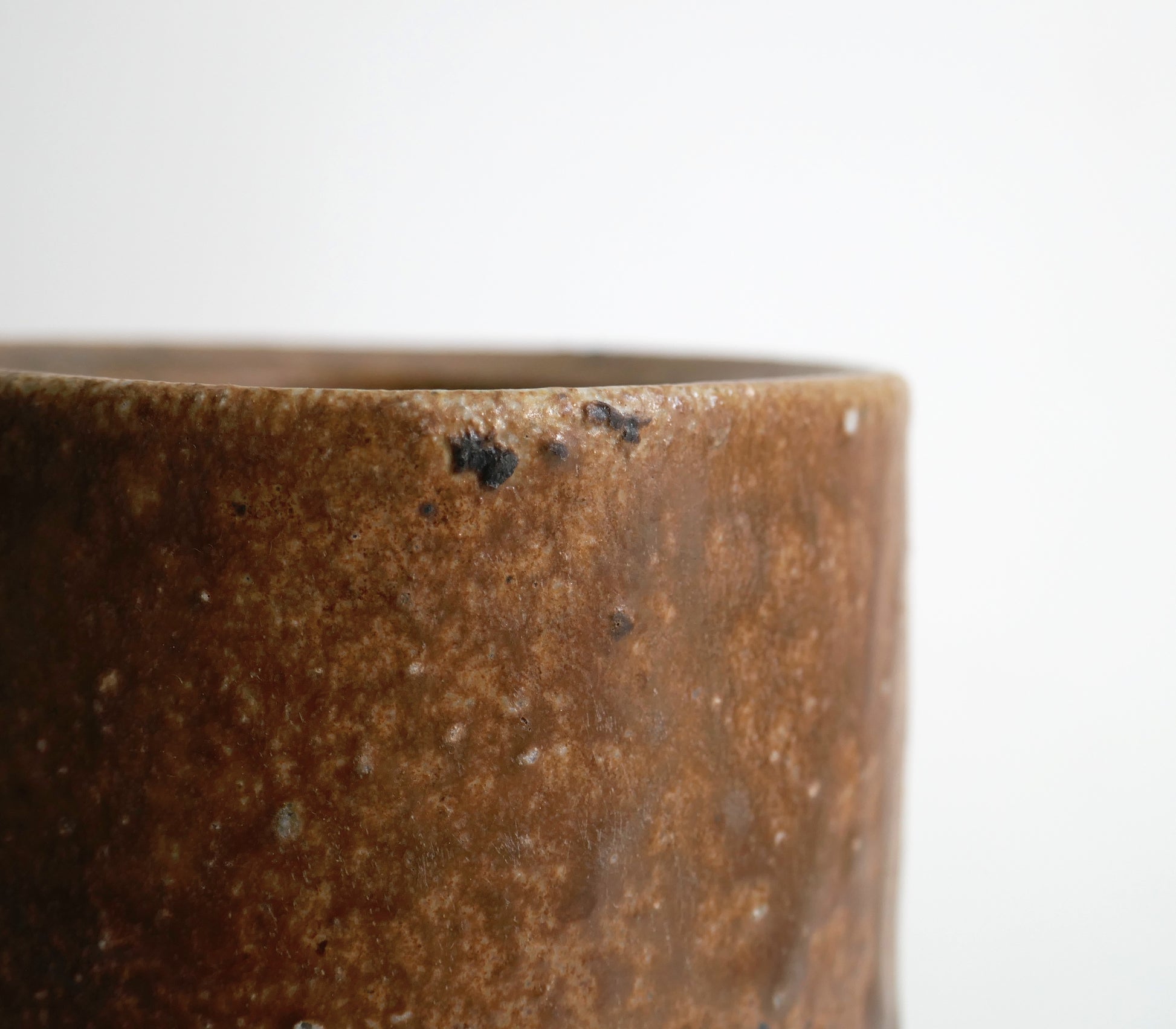 Gros plan sur la texture brune et minérale du bord d’un vase Bizen cuit au bois sans glaçure appliquée