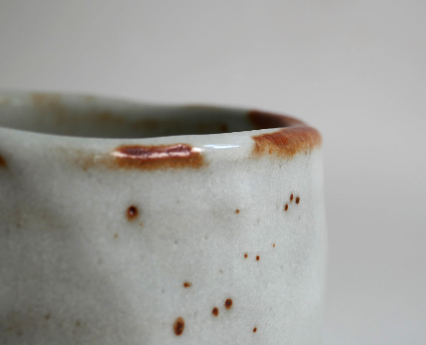 Gros plan sur le bord irrégulier du chawan Shino-yaki, émail blanc laiteux et nuances rouge brun typiques du Beni Shino japonais.