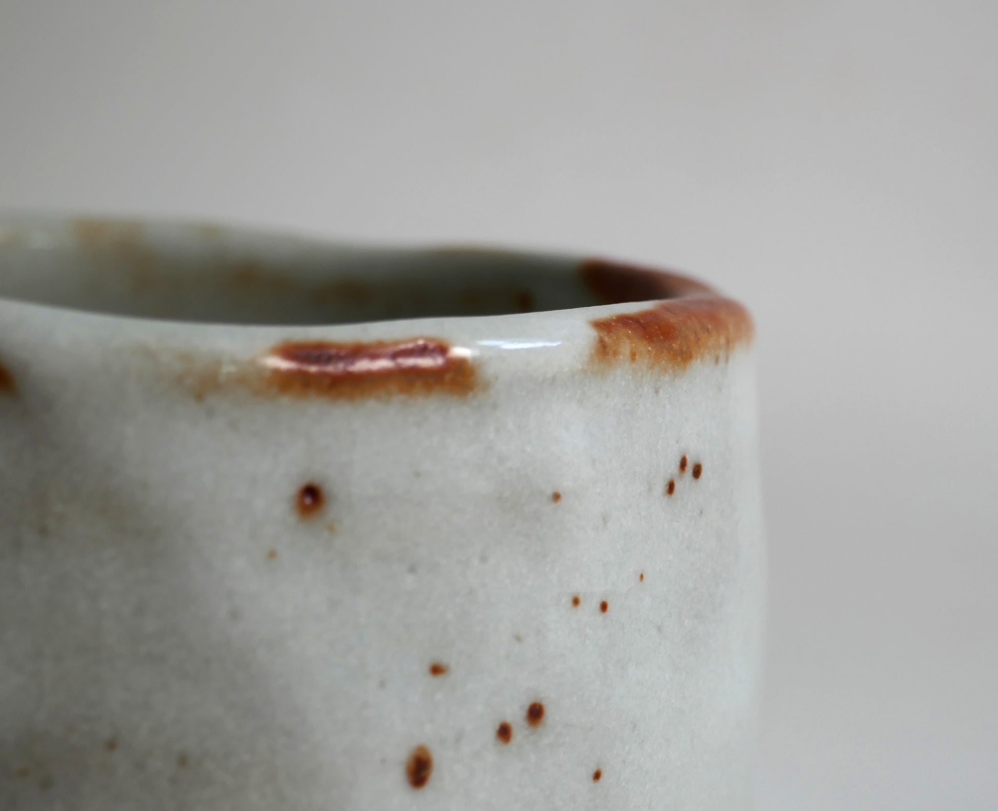 Gros plan sur le bord irrégulier du chawan Shino-yaki, émail blanc laiteux et nuances rouge brun typiques du Beni Shino japonais.