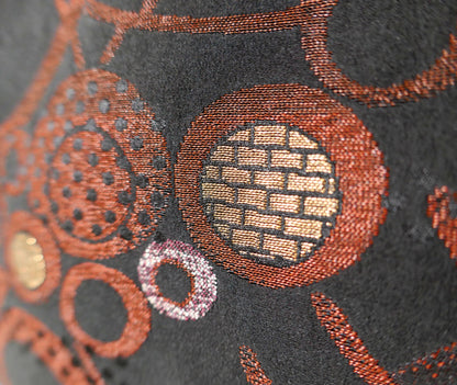 Détail d'un cercle géométrique doré et de motifs végétaux cuivrés sur le tissu en brocart de soie noire d'un haori traditionnel.