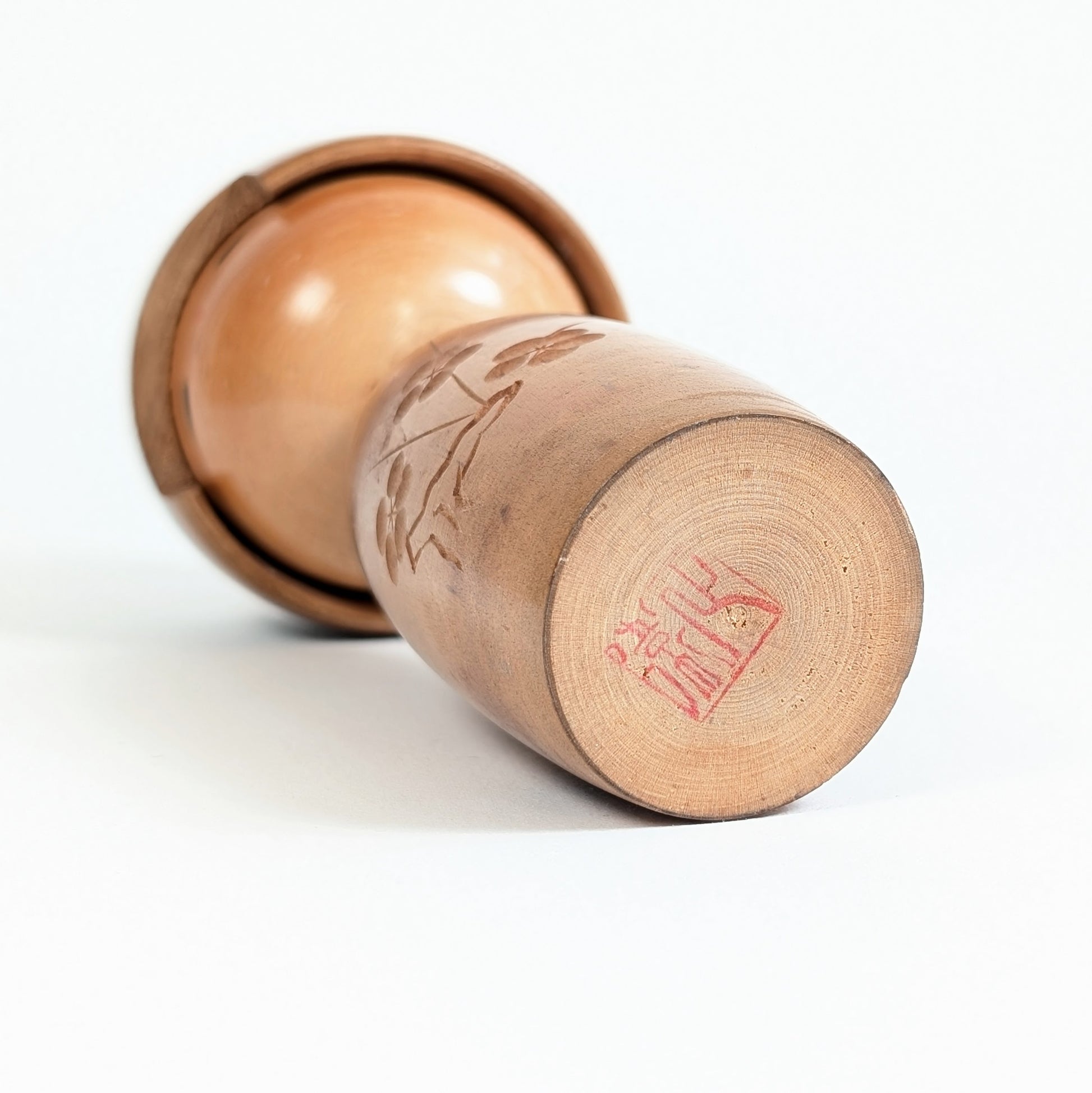 Dessous de la kokeshi japonaise Fujikawa montrant le cachet rouge de l’artisan sur le bois tourné
