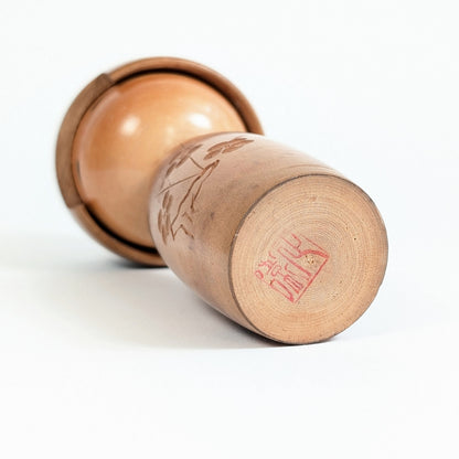 Dessous de la kokeshi japonaise Fujikawa montrant le cachet rouge de l’artisan sur le bois tourné
