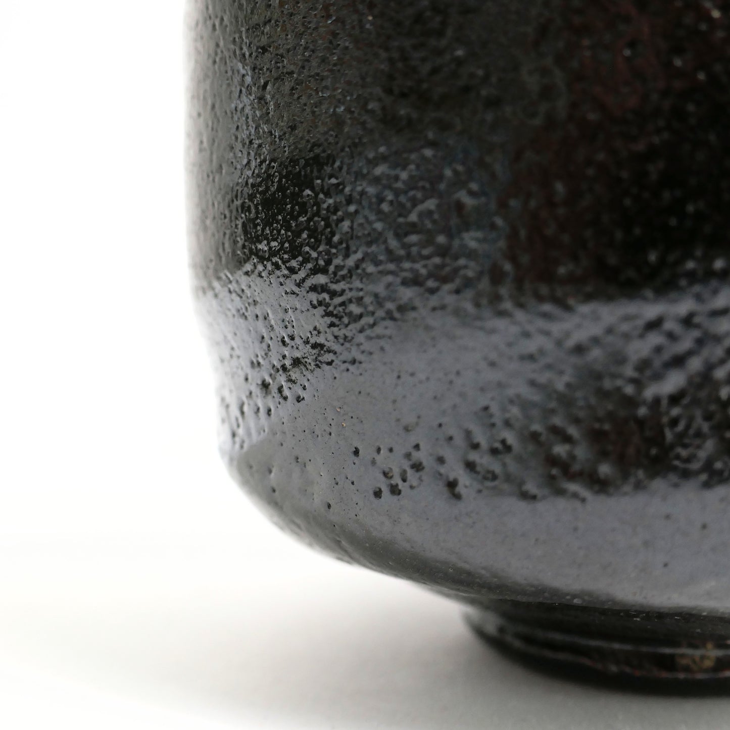Macro de l’émail noir texturé d’un chawan artisanal, révélant l’esthétique wabi-sabi de la céramique japonaise.
