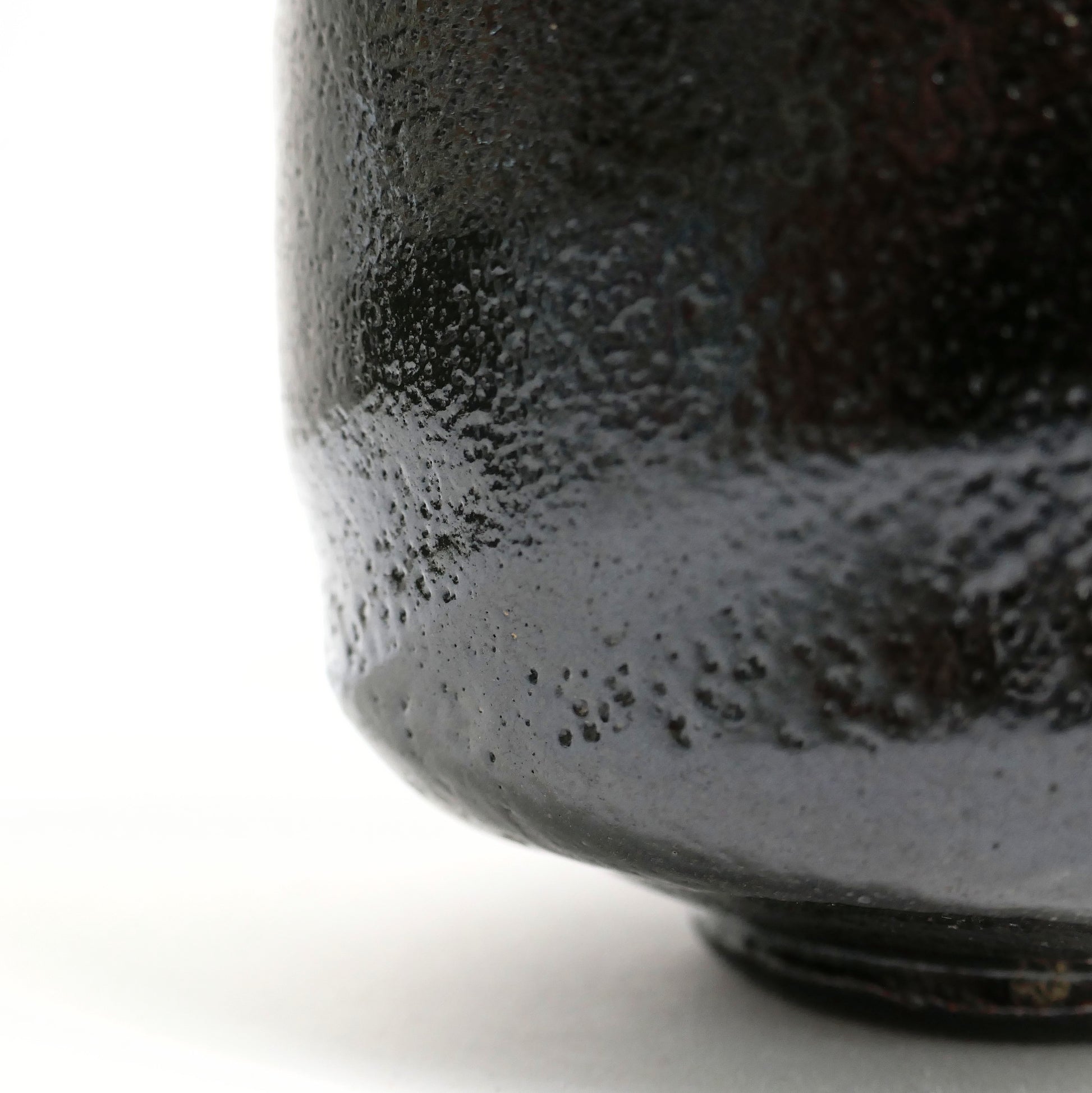 Macro de l’émail noir texturé d’un chawan artisanal, révélant l’esthétique wabi-sabi de la céramique japonaise.
