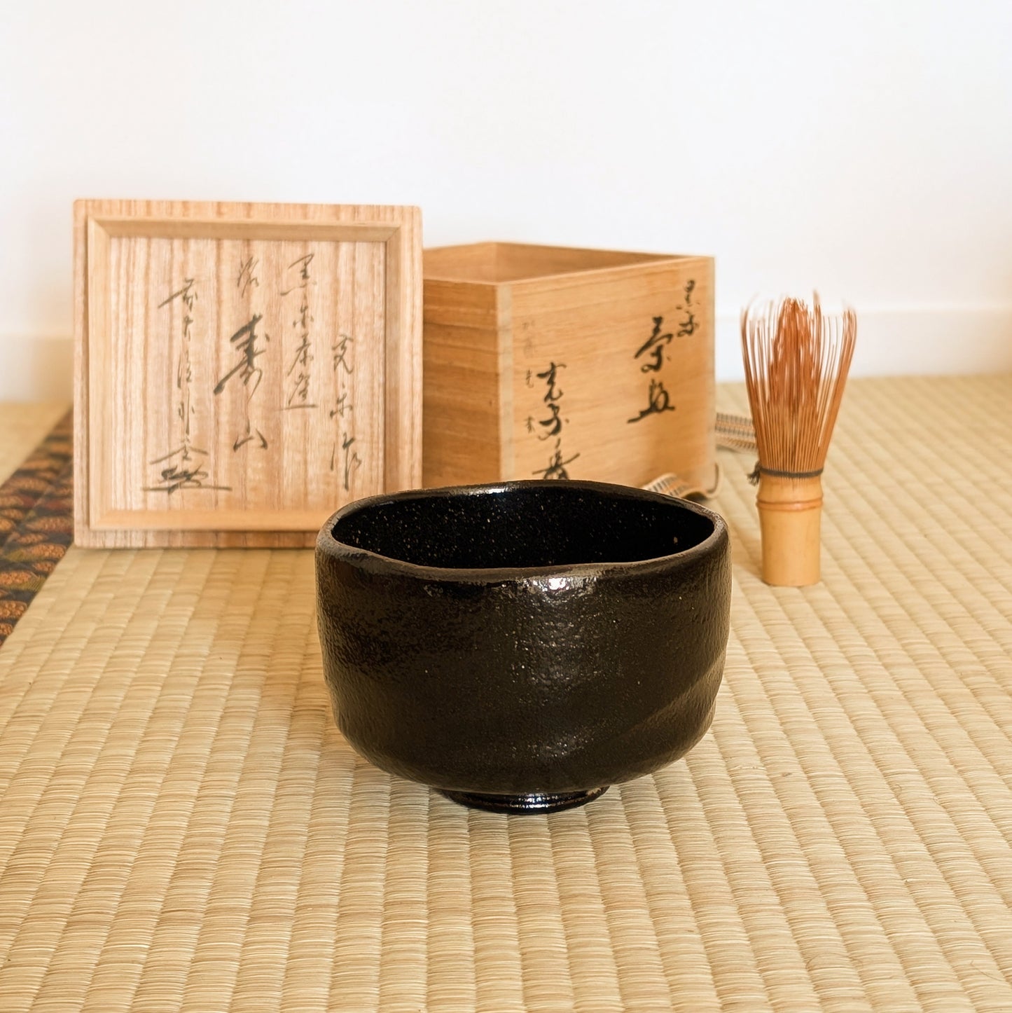 Mise en scène chanoyu sur tatami avec bol matcha noir, chasen en bambou et tomobako en bois de paulownia.
