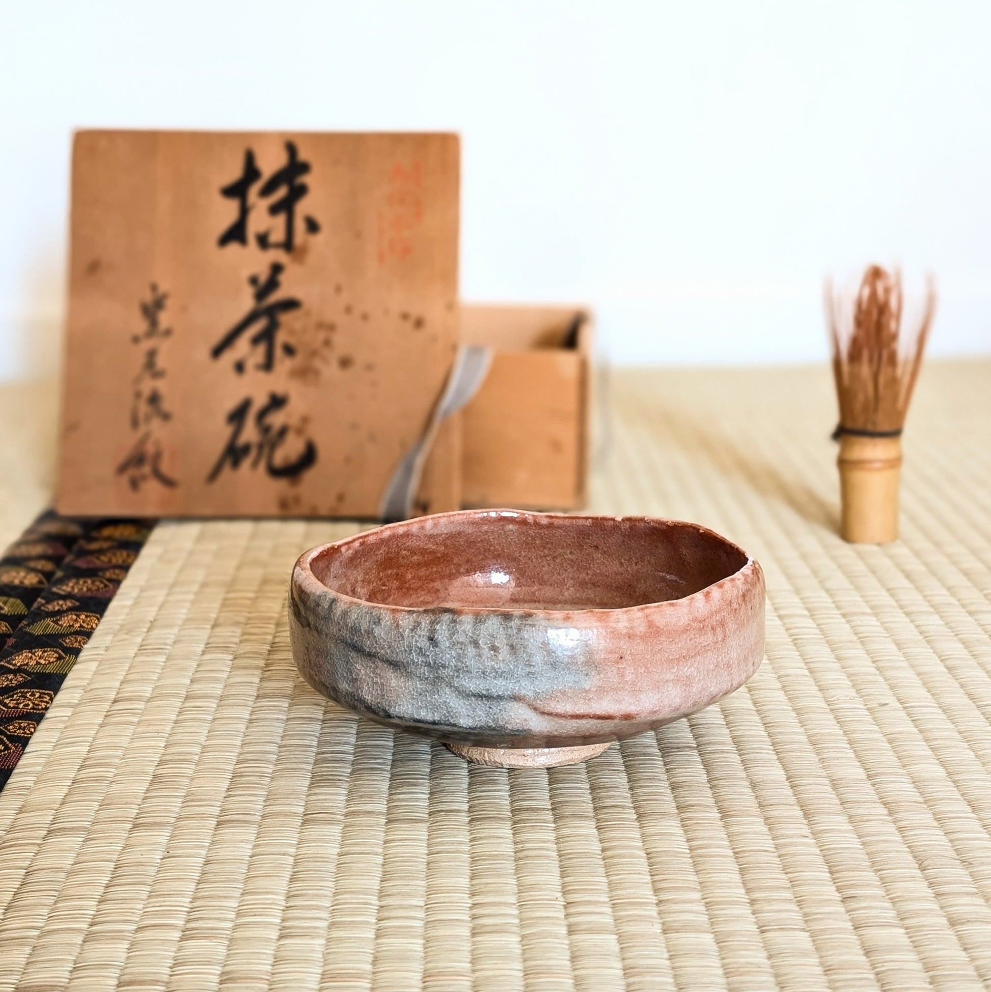Chawan aka raku rose modèle hirachawan posé sur tatami avec chasen et boîte bois pour cérémonie du thé japonaise