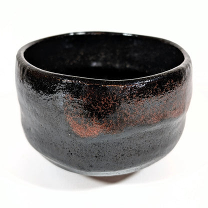 Bol à thé japonais en raku noir, œuvre artisanale de Sasaki Shoraku, photographié en vue oblique pour révéler les nuances de la glaçure.