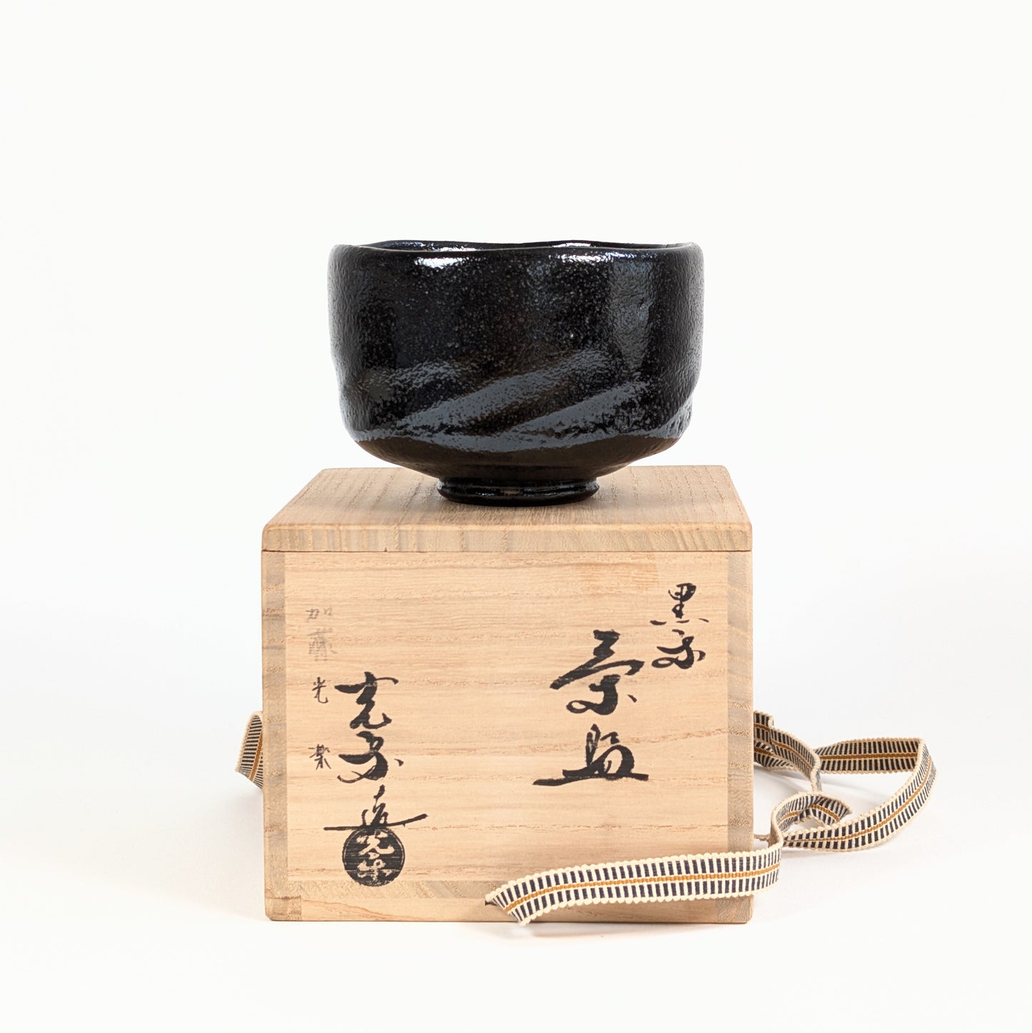Chawan kuro raku de Watanabe Kōraku 渡辺光楽 posé sur sa boîte tomobako calligraphiée pour la cérémonie du thé.
