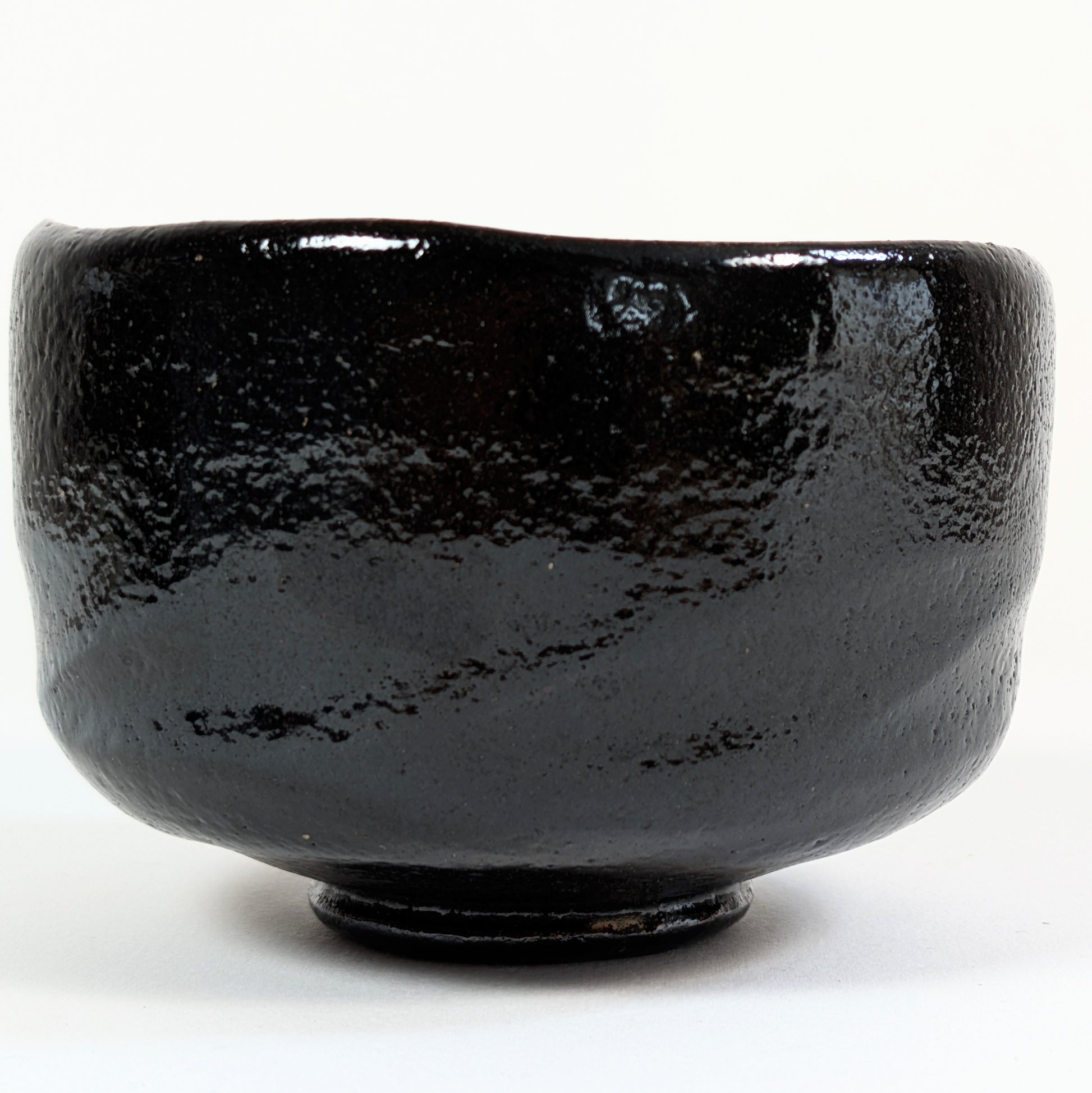 Chawan signé Watanabe Kōraku avec cachet 光楽 près du bord et glaçure kuro raku à la surface texturée.
