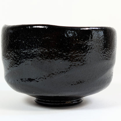 Chawan signé Watanabe Kōraku avec cachet 光楽 près du bord et glaçure kuro raku à la surface texturée.
