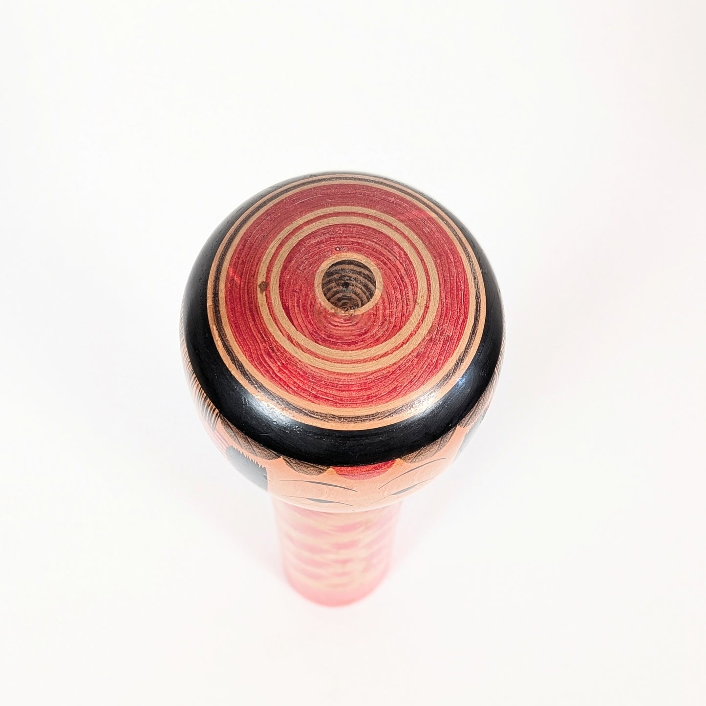 Vue du sommet de la kokeshi Yajirō avec coiffure janome, formée de cercles concentriques rouges, noirs et couleur bois.