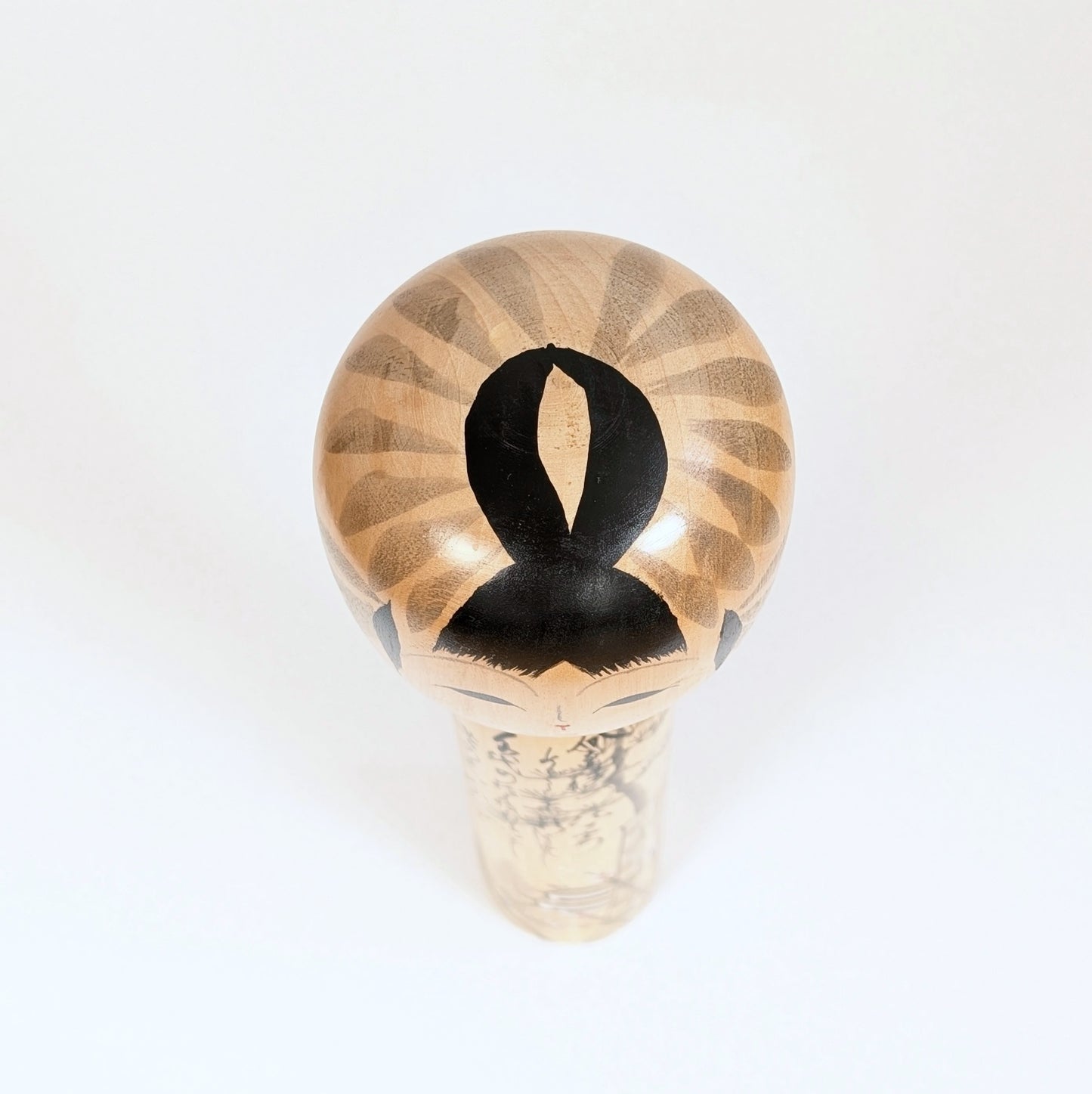 Vue du sommet de la tête de la kokeshi Shūhō, détail de la coiffure noire et du décor peint sur bois.