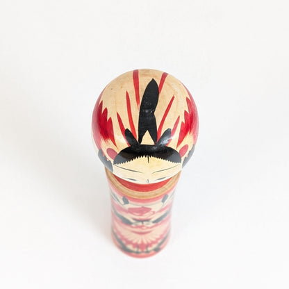 Vue du dessus de la tête d’une kokeshi Naruko de Suzuki Toshiyuki, montrant la coiffure noire et le décor rouge peint à la main.