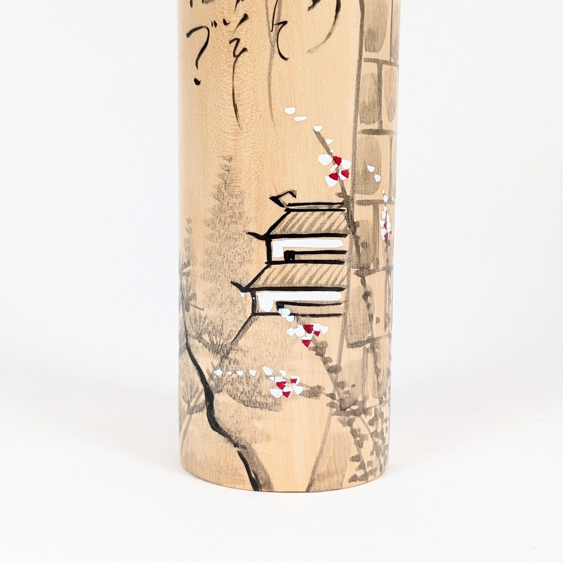 Détail du décor peint de la kokeshi Shūhō : château, branche fleurie et paysage japonais sur bois clair.