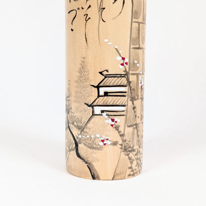 Détail du décor peint de la kokeshi Shūhō : château, branche fleurie et paysage japonais sur bois clair.