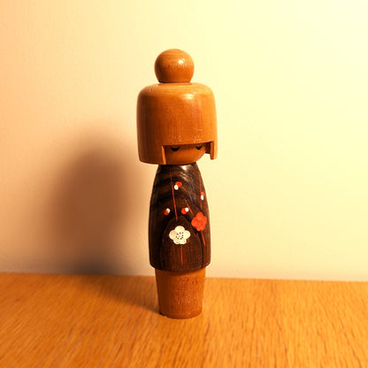 Kokeshi vintage japonaise Koigokoro de l'atelier Usaburo exposée sur un meuble en bois, dans une ambiance chaleureuse aux tons dorés, avec son kimono fleuri brun.