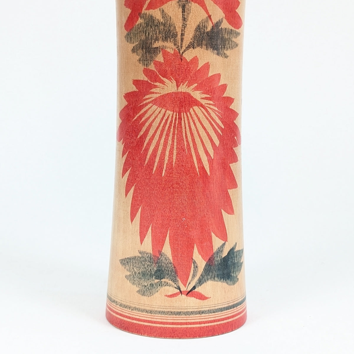 Gros plan sur le motif floral hishigiku d’une dento kokeshi Naruko, décor traditionnel rouge et noir sur bois tourné japonais.