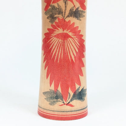 Gros plan sur le motif floral hishigiku d’une dento kokeshi Naruko, décor traditionnel rouge et noir sur bois tourné japonais.
