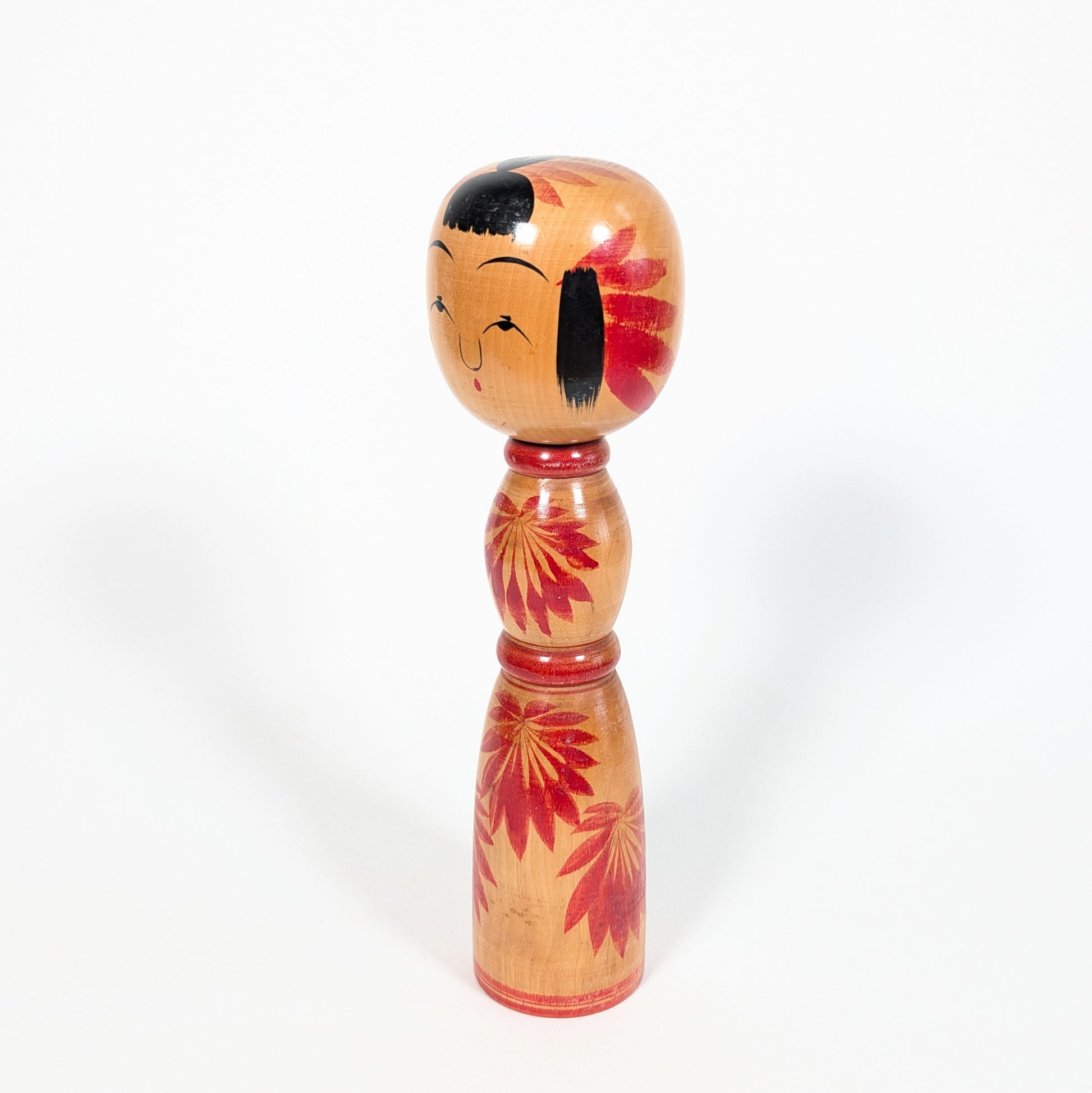 Dento kokeshi Yajirō par Hachihoya Kunio, vue de profil avec visage souriant, frange noire et motif chrysanthème rouge