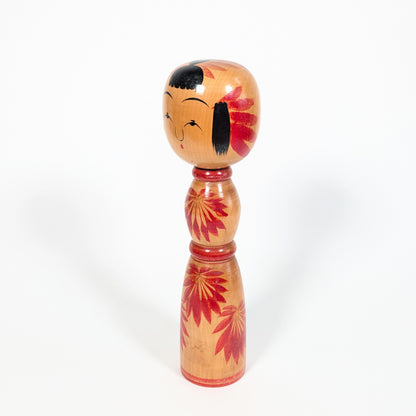 Dento kokeshi Yajirō par Hachihoya Kunio, vue de profil avec visage souriant, frange noire et motif chrysanthème rouge