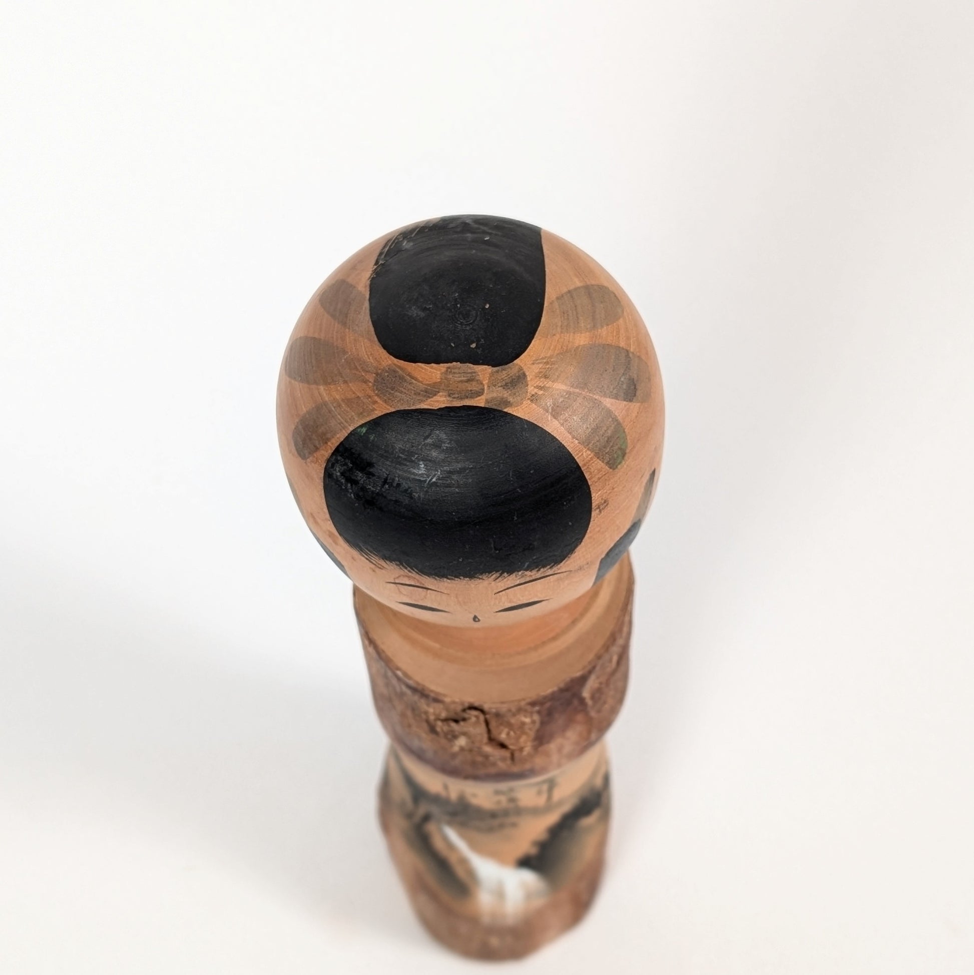 Vue du dessus de la tête d’une kokeshi omiyage Sato Kôson, avec coiffure traditionnelle noire et motifs peints à la main.