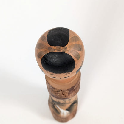 Vue du dessus de la tête d’une kokeshi omiyage Sato Kôson, avec coiffure traditionnelle noire et motifs peints à la main.