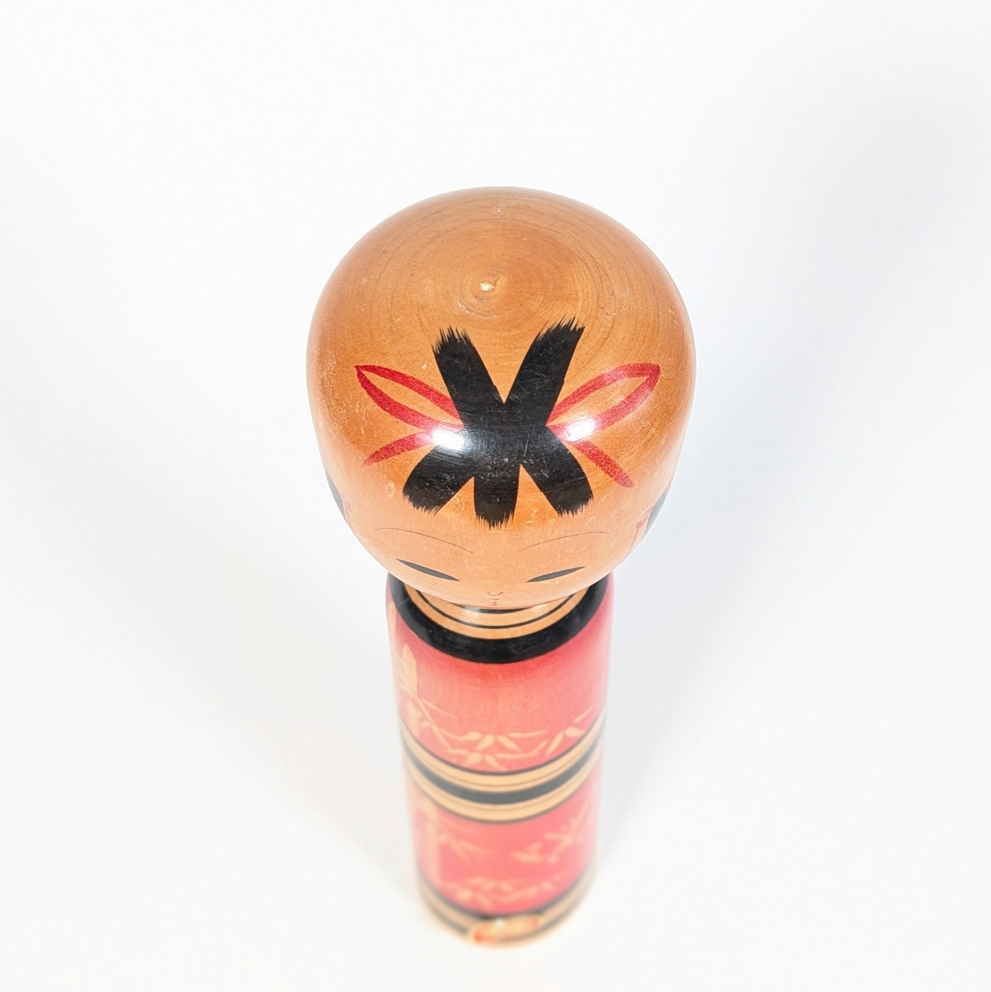 Vue du dessus de la tête d’une kokeshi sosaku avec coiffure noire et ornements rouges peints