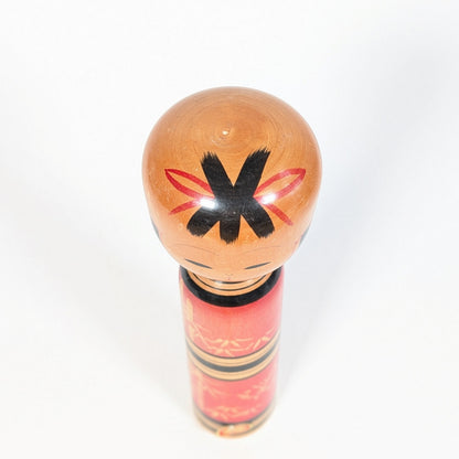 Vue du dessus de la tête d’une kokeshi sosaku avec coiffure noire et ornements rouges peints