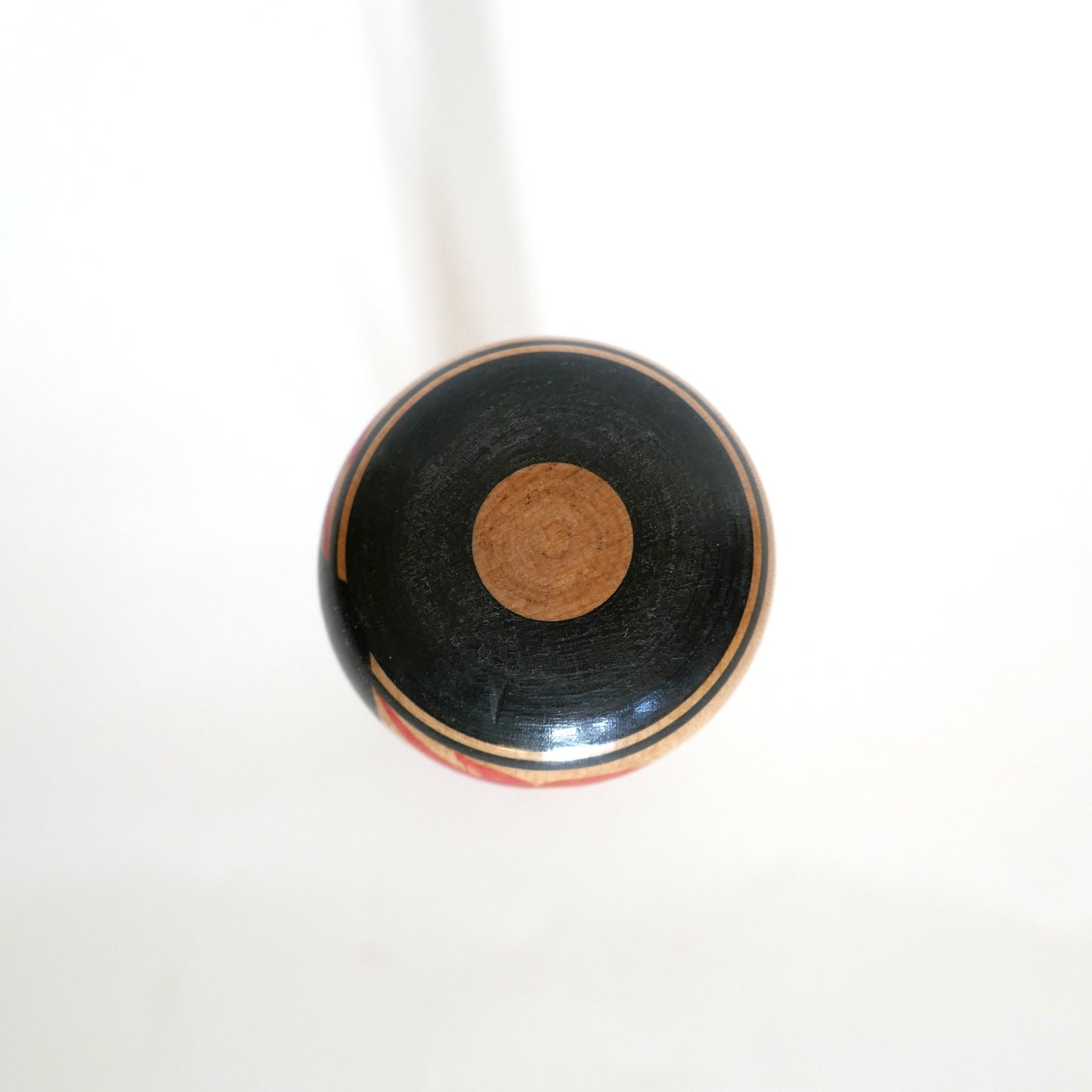 Vue du dessus de la tête d’une kokeshi Tsuchiyu présentant un motif Janome, dit œil de serpent rouge, typique de cette lignée artisanale.