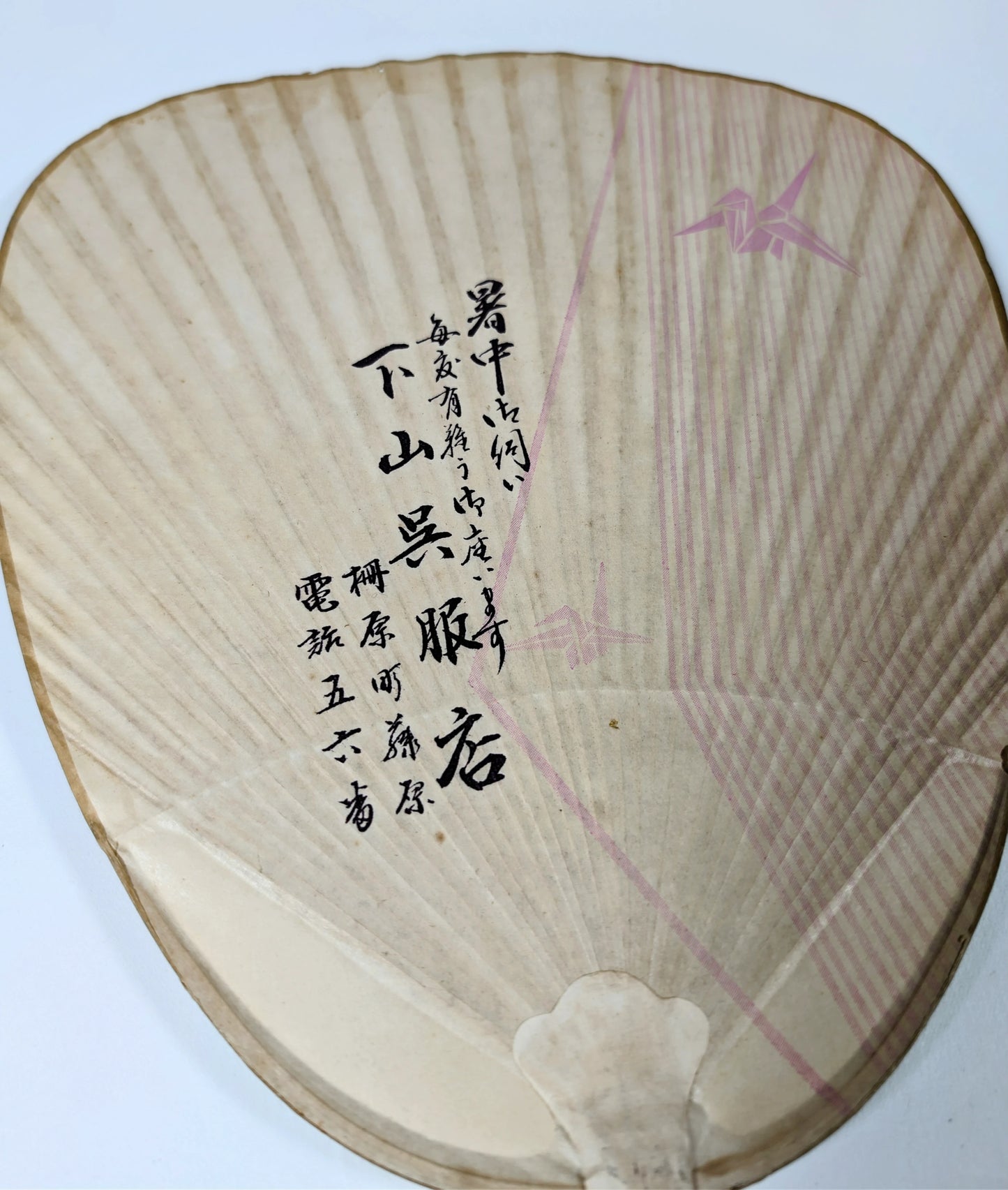 gros plan sur la calligraphie japonaise au dos d’un éventail uchiwa publicitaire de l’ère Shōwa