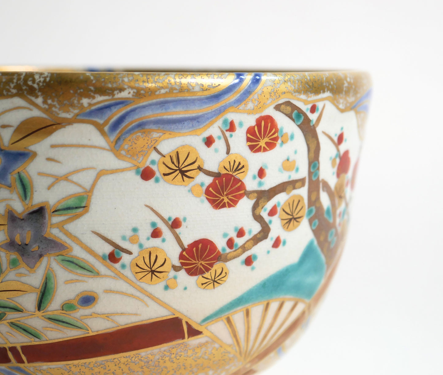 Gros plan du décor iro-e du chawan, avec branche de prunier ume, campanules kikyō, vagues bleues et rehauts d’or.