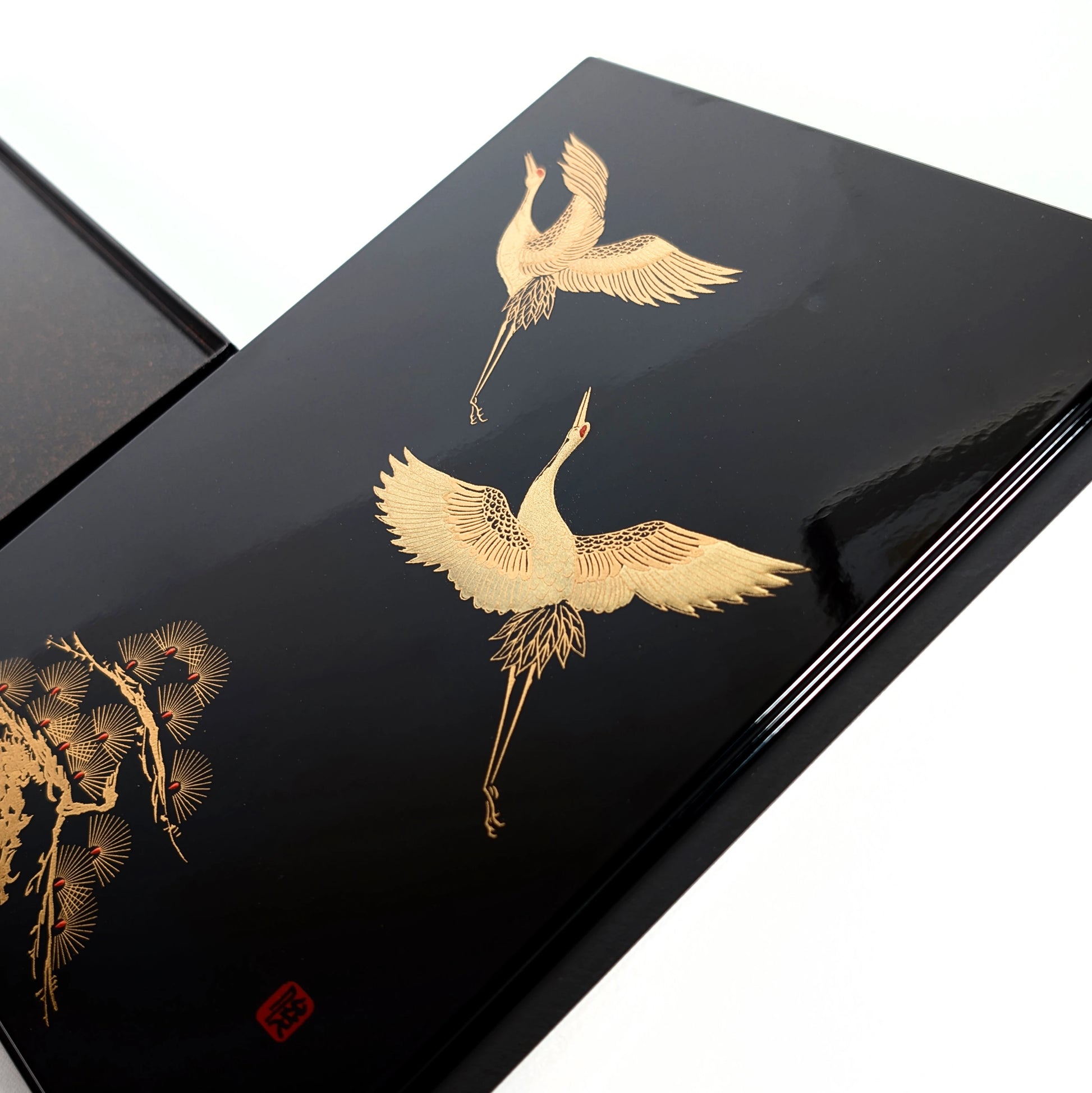 Gros plan sur une grue tsuru dorée en maki-e, ailes déployées sur fond de laque noire.