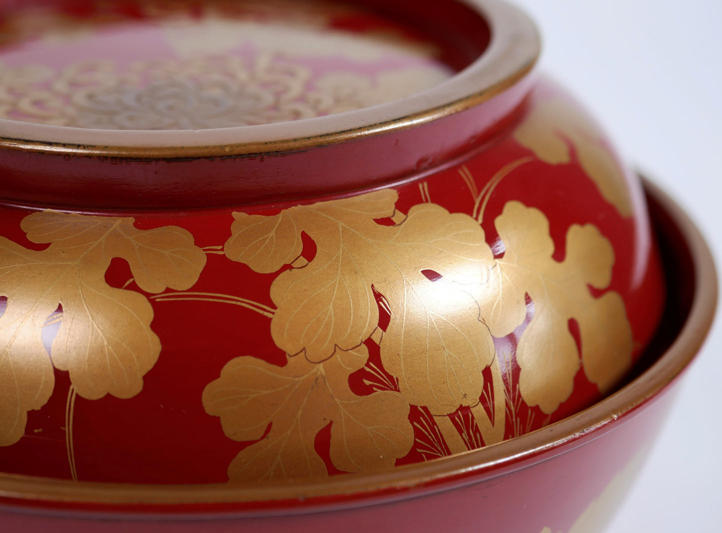 Gros plan sur les feuilles de chrysanthème kiku en maki-e doré, avec fines nervures sur laque urushi rouge brillante.