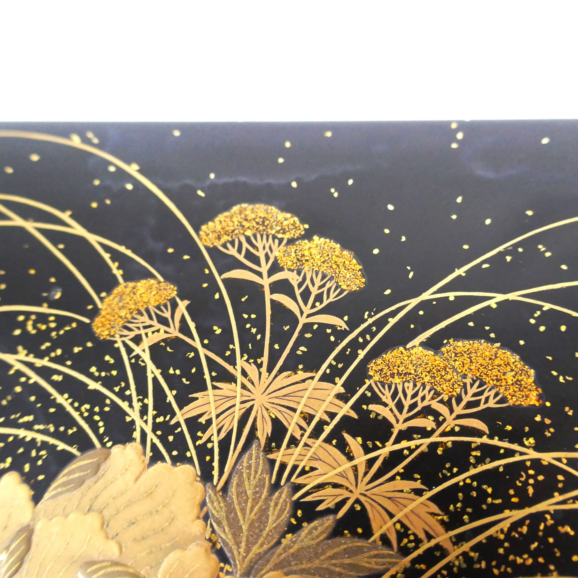 Détail de fleurs jaunes en maki-e sur boîte en laque noire japonaise signée Zohiko Kyoto, décor raffiné or et paillettes.