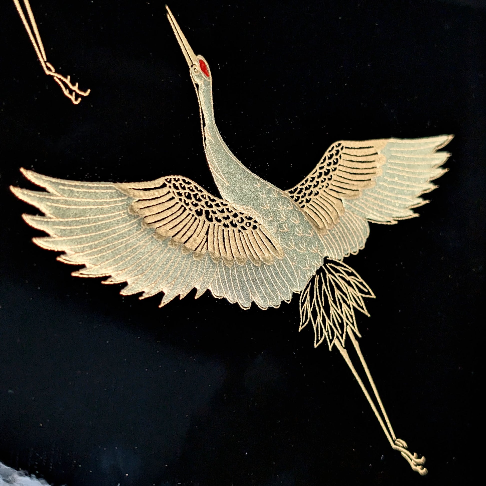 Détail d’une grue dorée réalisée en maki-e sur laque urushi noire, plumage finement gravé.
