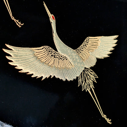 Détail d’une grue dorée réalisée en maki-e sur laque urushi noire, plumage finement gravé.