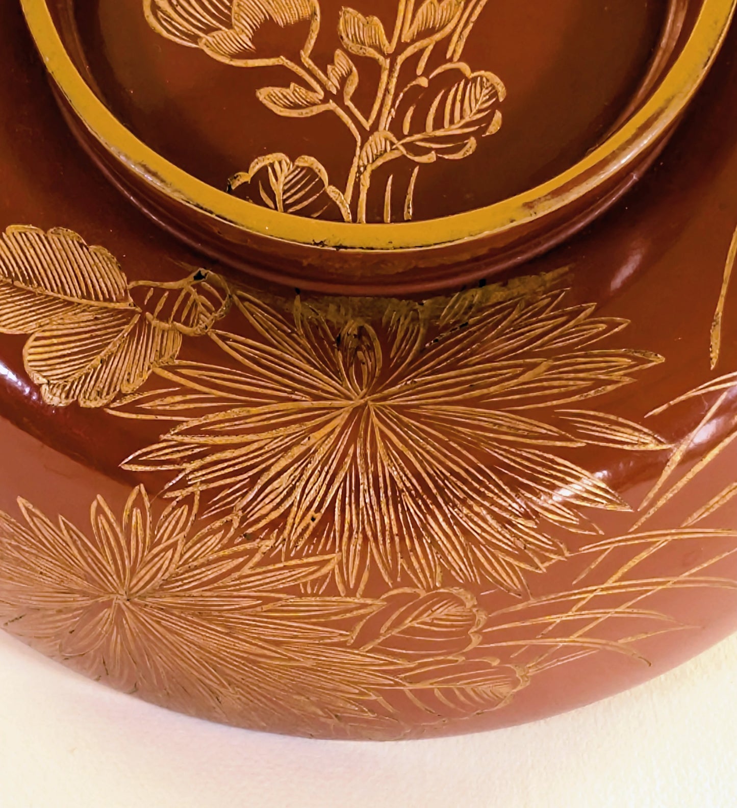 Gros plan sur un motif maki-e représentant un chrysanthème stylisé sur un bol en laque japonaise ancienne.