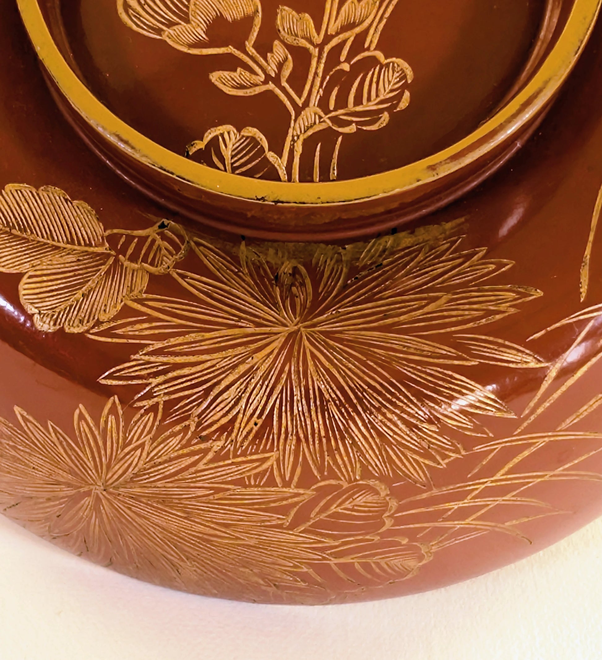 Gros plan sur un motif maki-e représentant un chrysanthème stylisé sur un bol en laque japonaise ancienne.