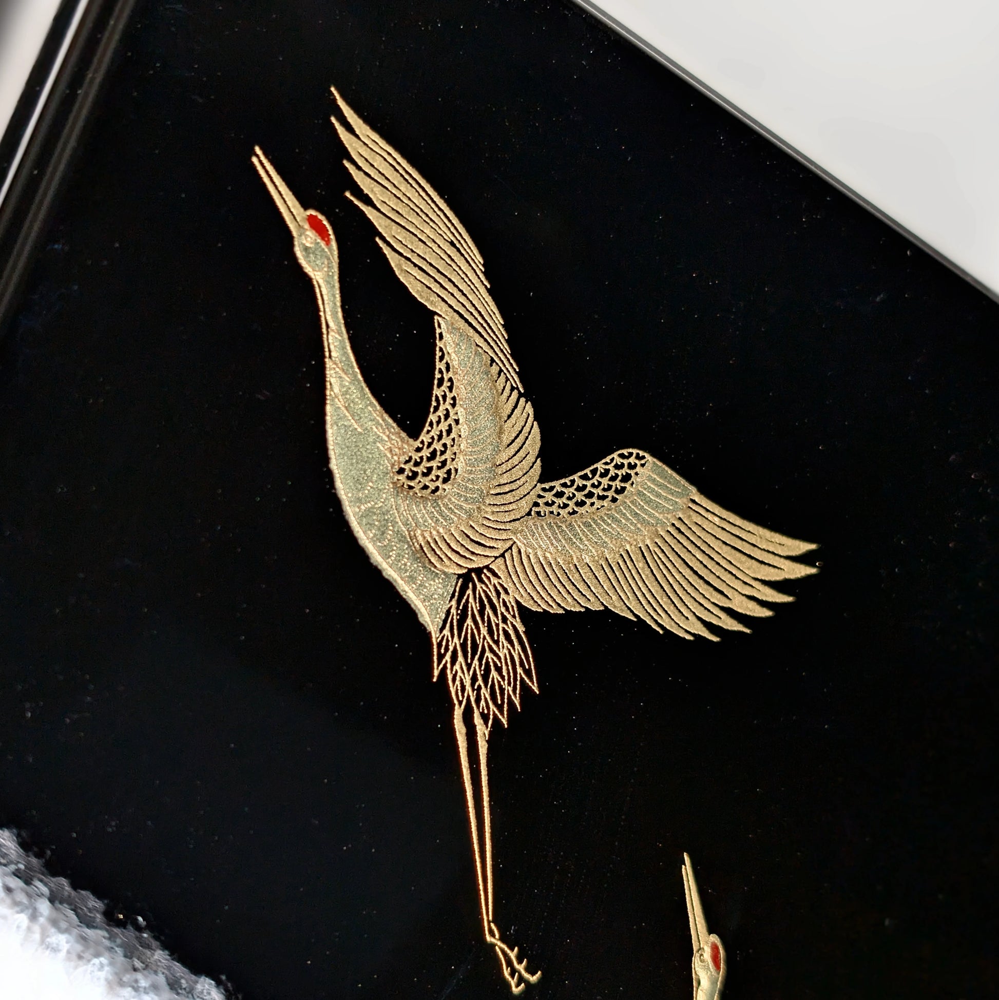 Détail d’une grue dorée (tsuru) en maki-e, ailes déployées sur fond laqué noir.