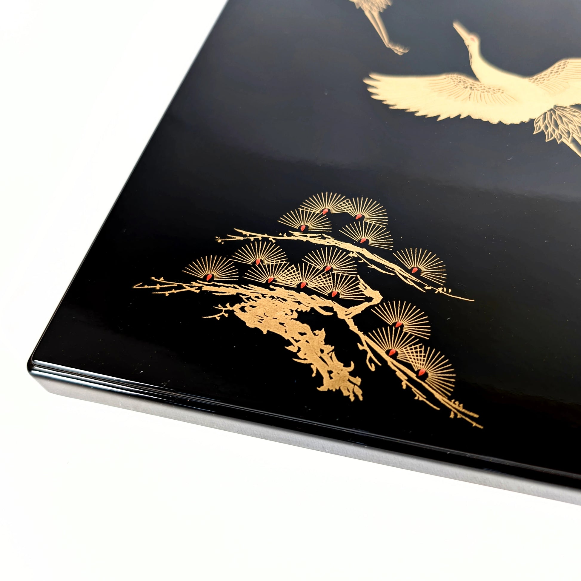 Gros plan sur le motif pin stylisé doré sur laque noire (maki-e et effet nashiji).