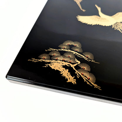 Gros plan sur le motif pin stylisé doré sur laque noire (maki-e et effet nashiji).