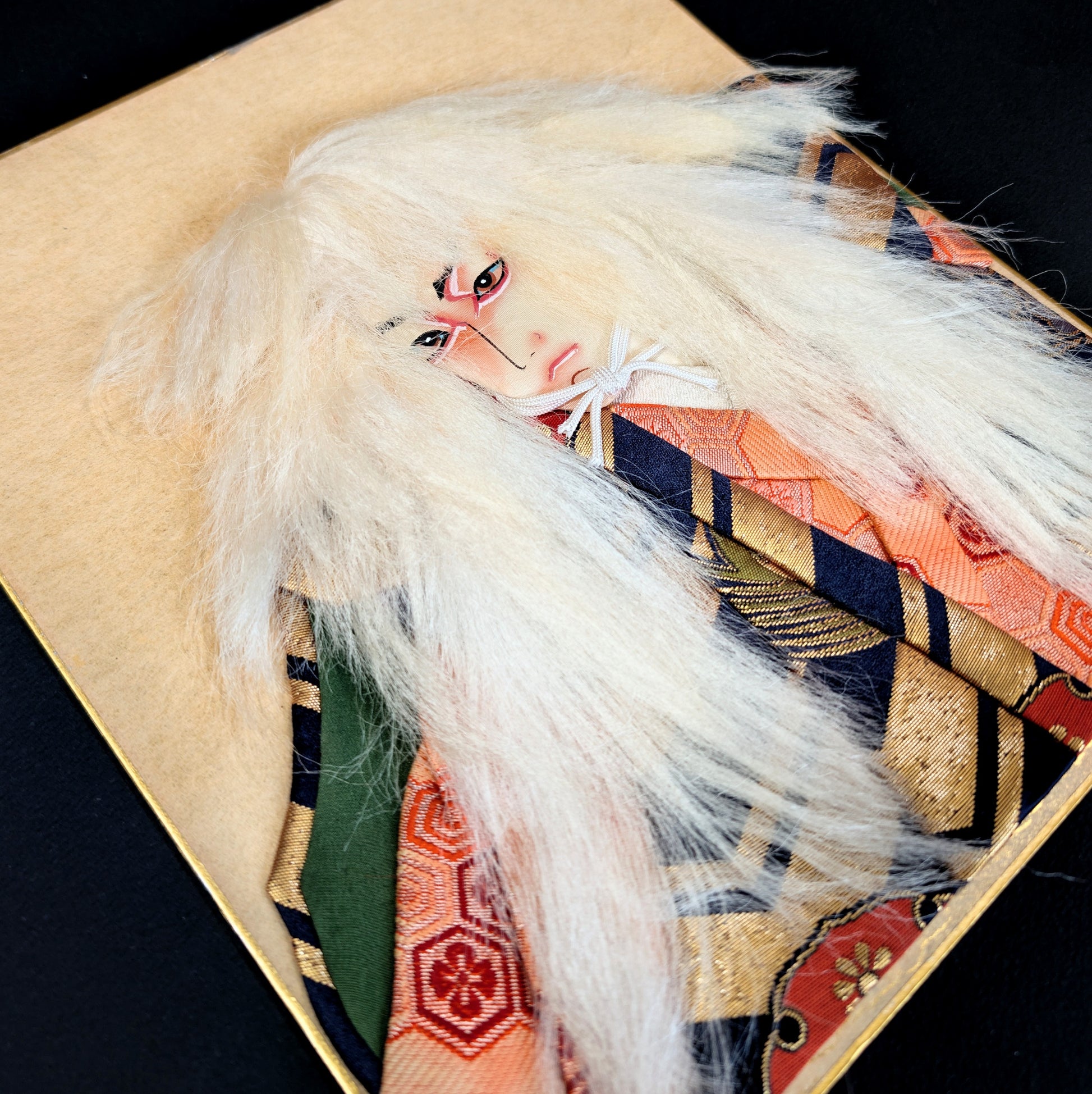 Détail d’un oshi-e kabuki avec maquillage kumadori et cheveux blancs, art textile japonais en relief objet de collection