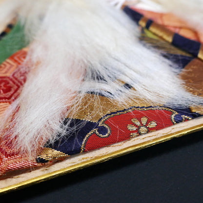 Détail textile d’un oshi-e japonais représentant un acteur kabuki, brocart de costume traditionnel et cheveux blancs en relief, artisanat japonais ancien de collection
