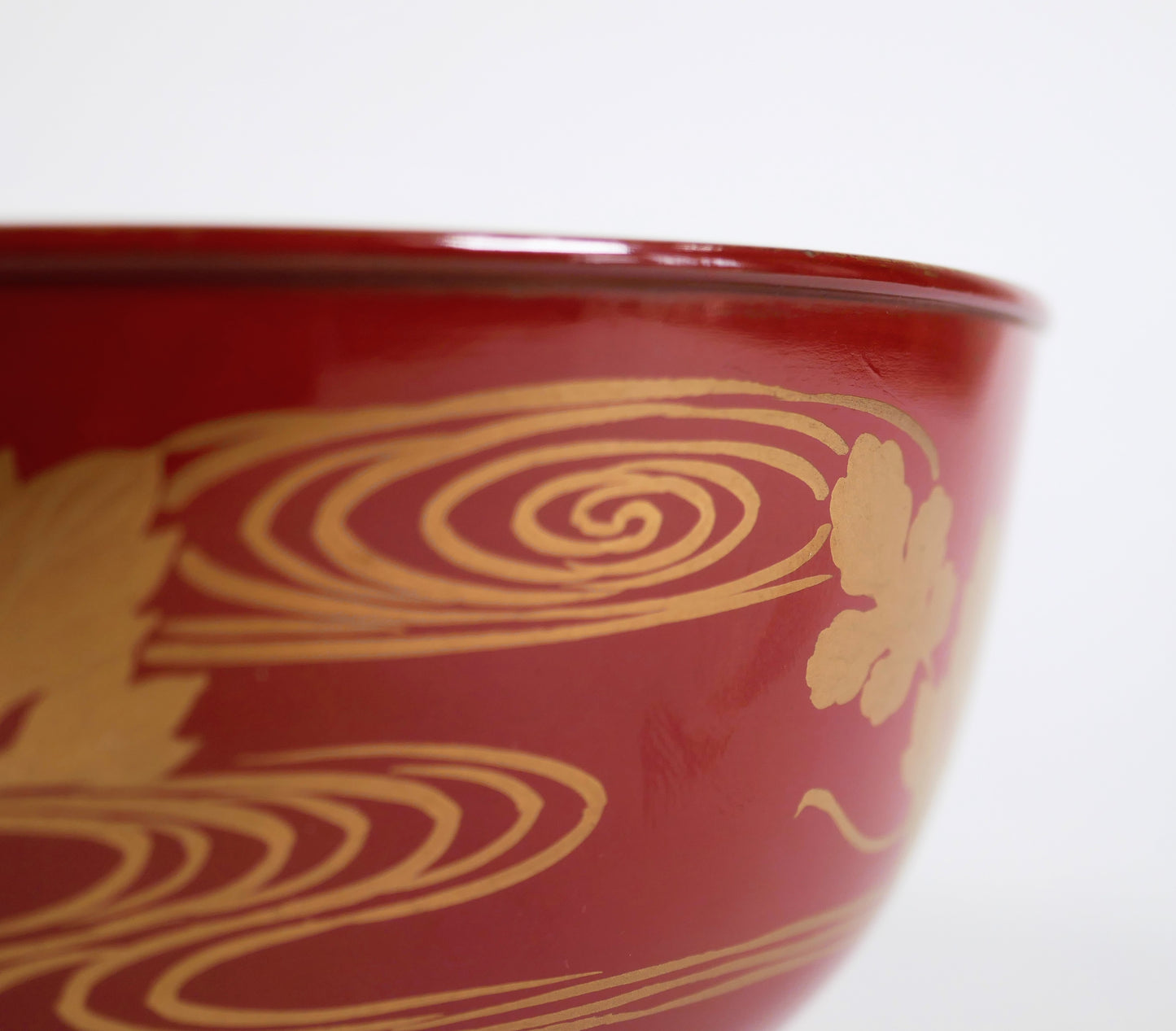 Gros plan sur les motifs japonais d’eau courante ryūsui tracés en maki-e doré sur la laque rouge du bol.