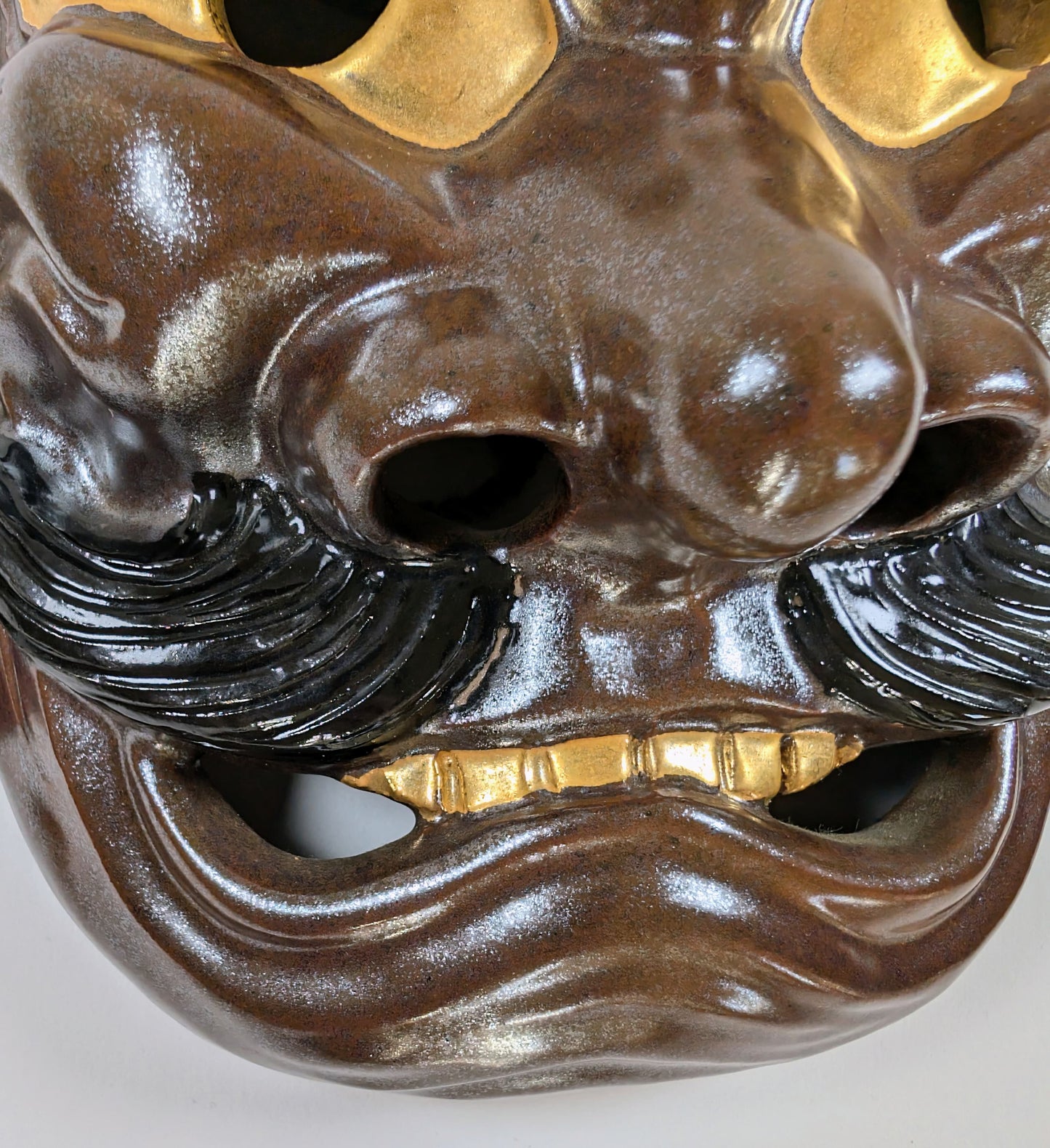 Gros plan sur le visage du masque Nô de Susanoo en céramique Kutani : moustache sculptée, nez saillant, dents dorées