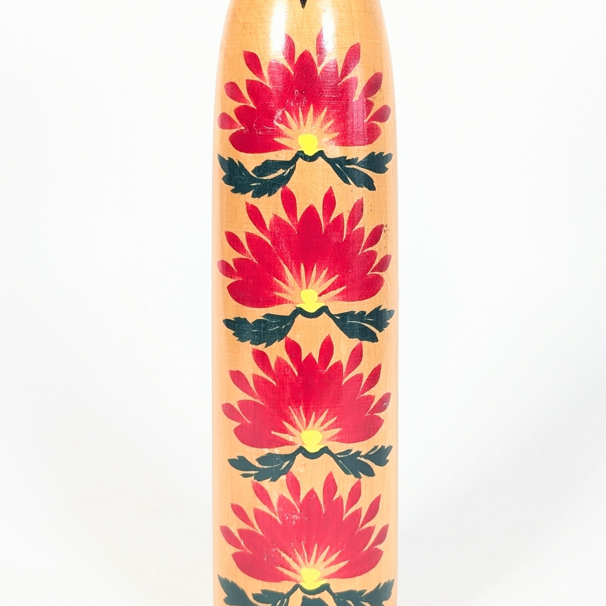 Détail des motifs kasane giku sur une kokeshi japonaise, grands chrysanthèmes rouges avec centres jaunes et feuilles vertes.