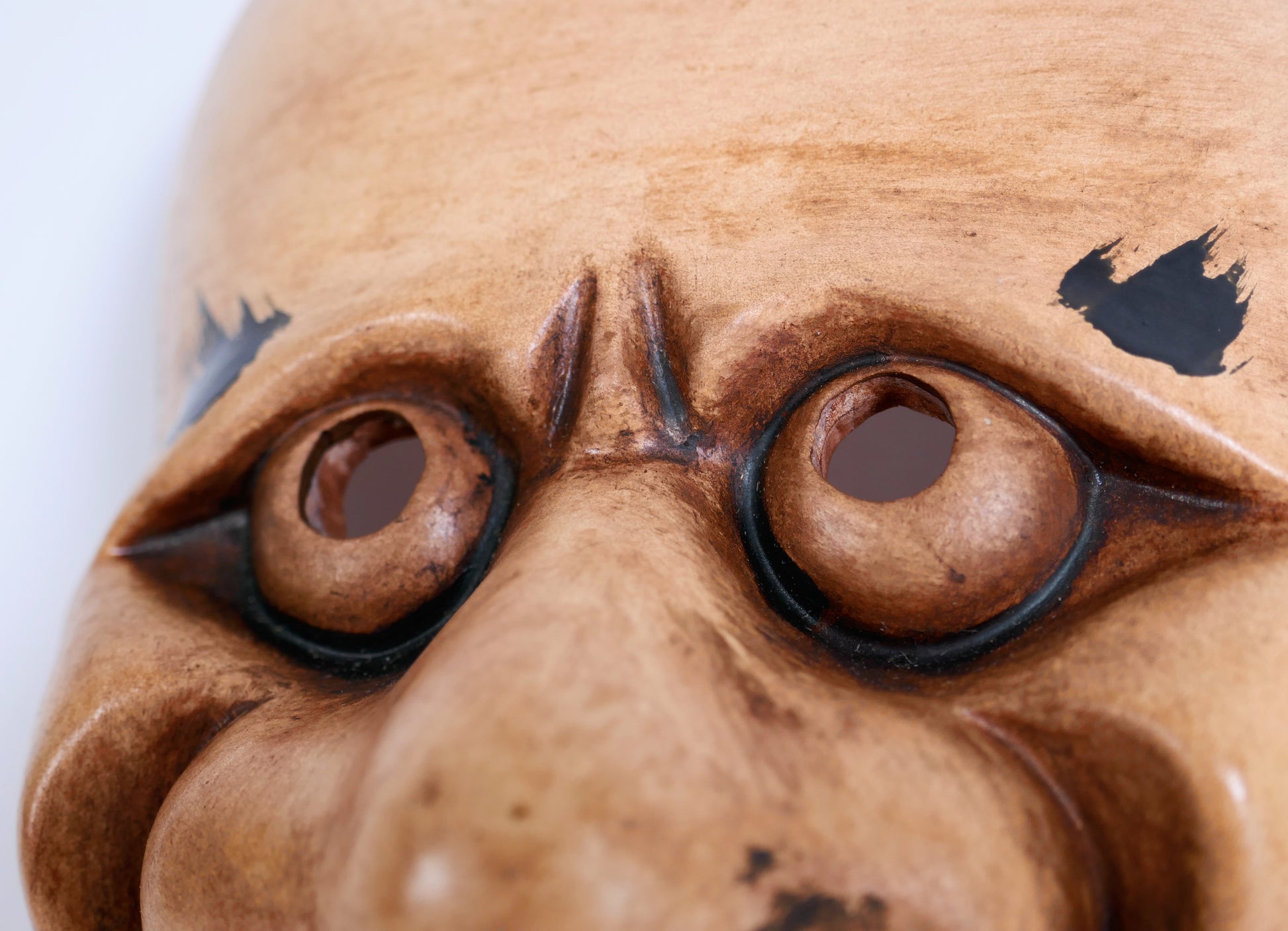 Détail des yeux ronds et des sourcils noirs d’un masque Noh Chōrei Beshimi, objet d’art japonais artisanal en céramique
