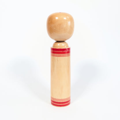 Dos d’une kokeshi shingata en bois naturel verni avec fines bandes rouges traditionnelles