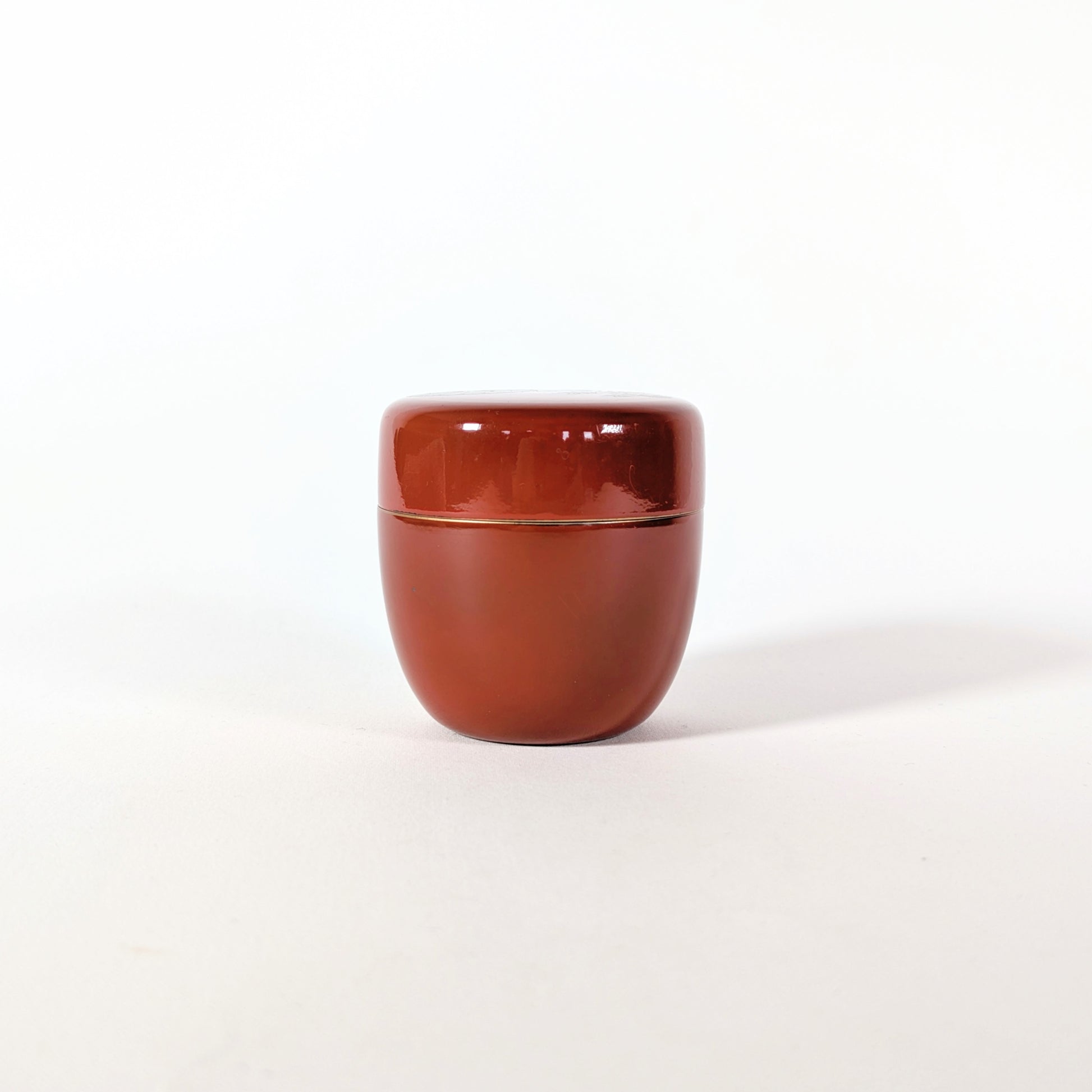 Vue arrière sobre d’un natsume vintage japonais en laque rouge brillante, petite boîte à matcha pour cérémonie du thé